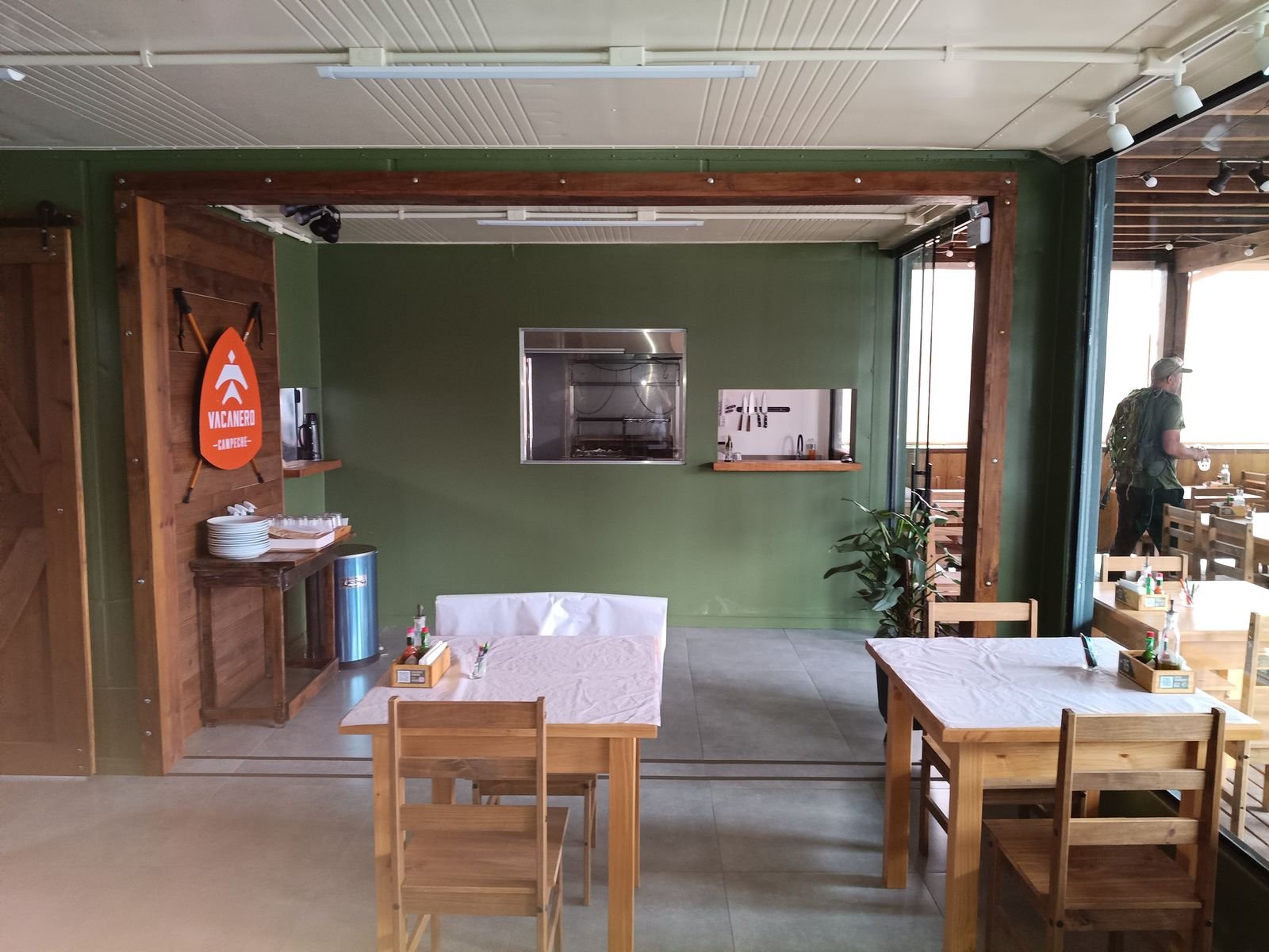 Salão do restaurante pronto, com mesas de madeira e parede verde